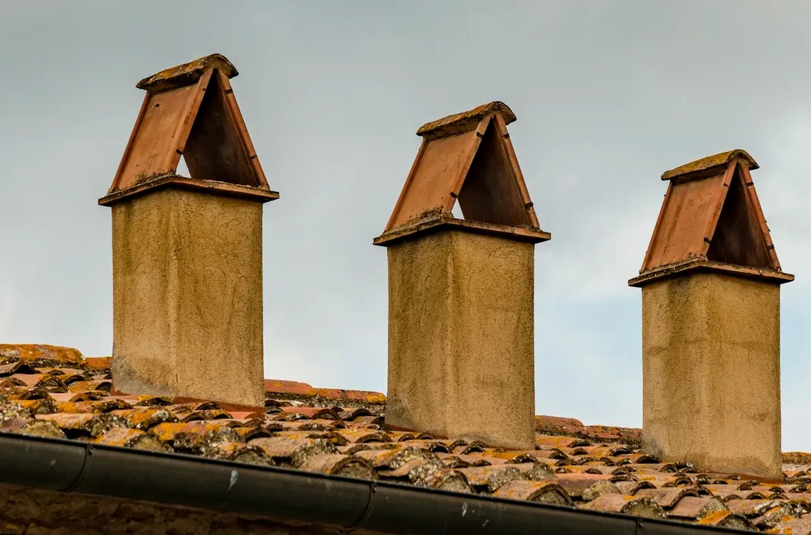 Xemeneies i sortides de ventilació sobre un vessant de teula, amb els seus remats